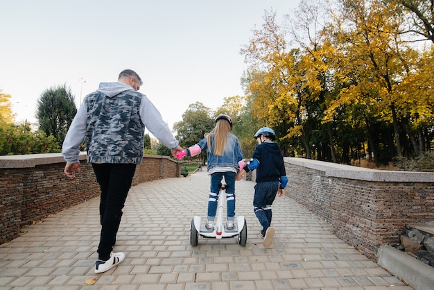 Un padre ayuda y enseña a sus hijos pequeños a andar en Segway en el parque durante la puesta de sol