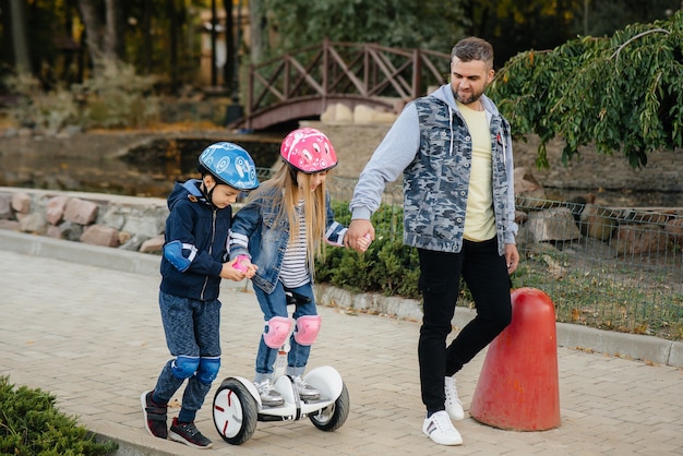 Un padre ayuda y enseña a sus hijos pequeños a montar en Segway en el parque durante la puesta de sol.