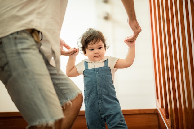 El padre ayuda a los niños a caminar, la familia de la infancia con el pequeño y lindo hijo del niño pequeño, el aprendizaje feliz en el primer paso con el apoyo del padre en casa