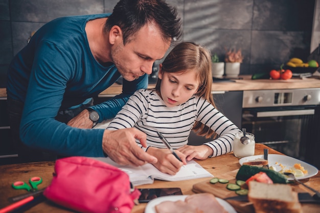 Padre ayudando a la hija con la tarea en la cocina