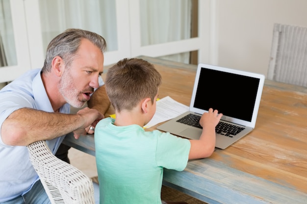 Padre ayudando a hijo mientras usa la computadora portátil en el escritorio