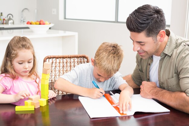 Padre ayudando a hijo con la tarea con la niña jugando con bloques en casa en la cocina