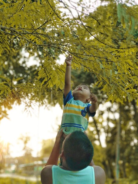 Foto padre ayudando a su hijo a alcanzar el árbol