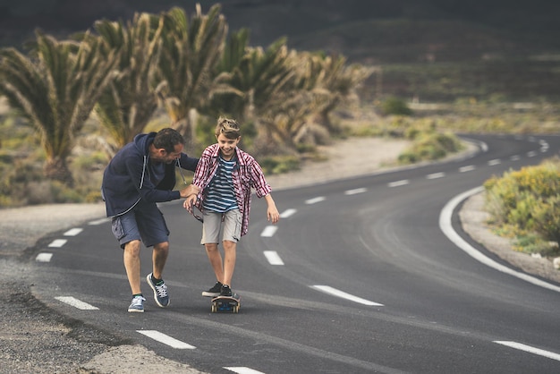 Foto padre ayudando a su hijo en el patinaje en la carretera contra las plantas