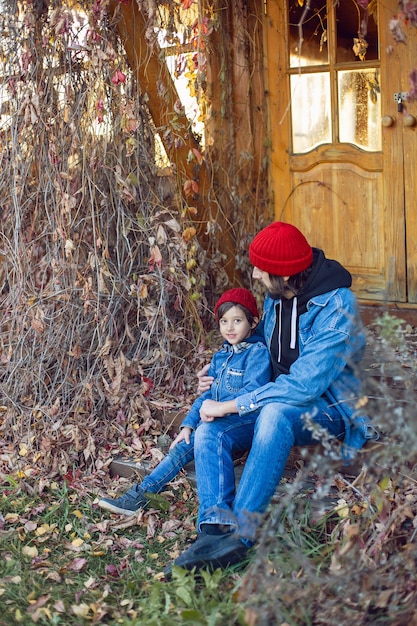 Padre con barba y su hijo con sombreros de punto rojos están sentados en el porche de la casa en Ivy en otoño