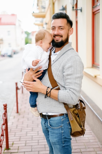 Un padre barbudo con gafas sostiene a un niño y sonríe Retrato de familia en la ciudad Padre con un niño de paseo