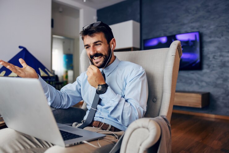 Foto padre barbudo guapo joven vestido elegante sentado en una silla en casa y usando la computadora portátil para la conferencia telefónica.