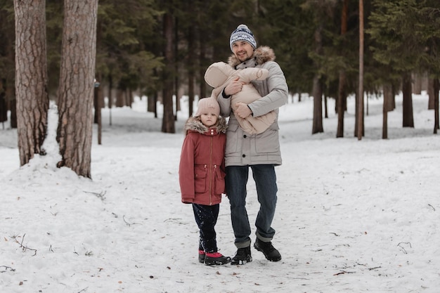 Padre camina con sus pequeñas hijas en el bosque de invierno