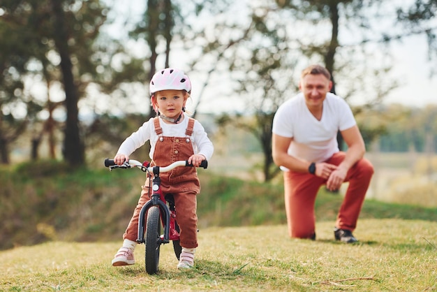 Padre con camisa blanca enseñando a su hija a andar en bicicleta al aire libre