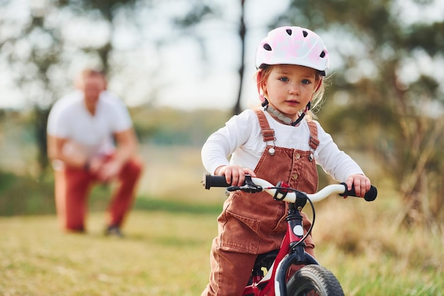 Padre con camisa blanca enseñando a su hija a andar en bicicleta al aire libre