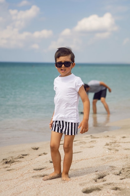 Padre con una camiseta a rayas camina con su hijo en pantalones cortos y una camiseta caminando por la playa en verano durante unas vacaciones