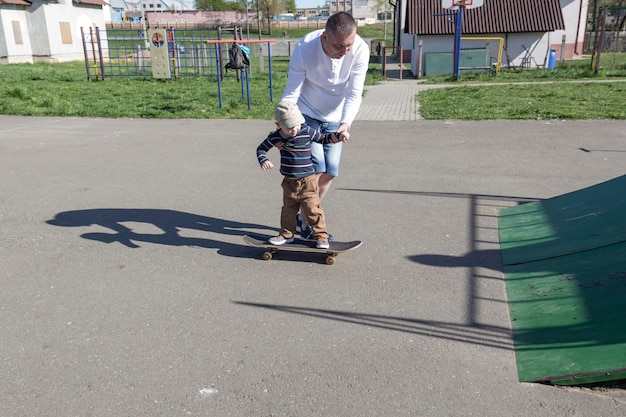 Un padre cariñoso y cariñoso le enseña a su hijo de tres años a andar en patineta