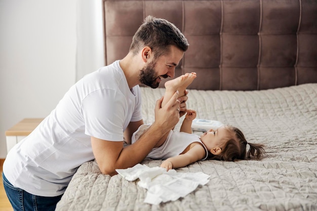 Un padre cariñoso está cambiando los pañales de su hija y jugando con sus pies