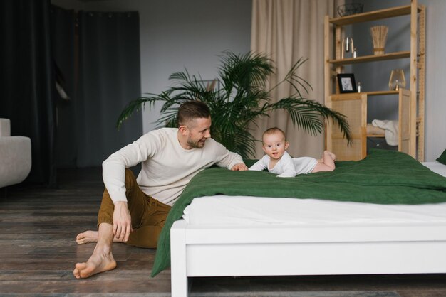 Padre caucásico jugando con un lindo bebé en la cama en casa Familia feliz atractivo papá guapo mira a su pequeño hijo acostado en la cama