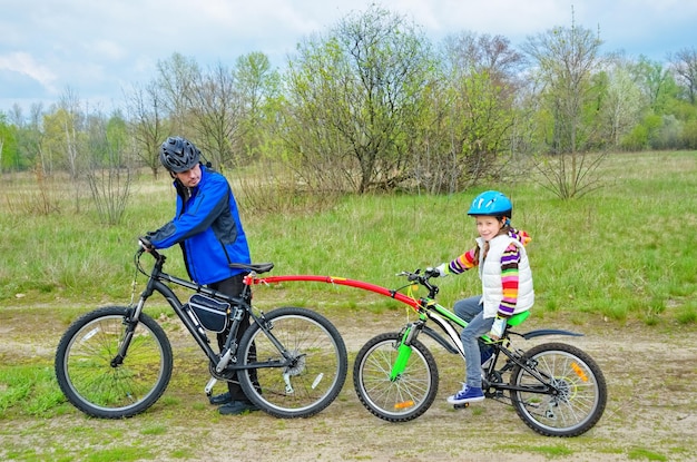 El padre ciclista familiar enseña al niño a andar en bicicleta con el deporte familiar de la barra de remolque de bicicletas