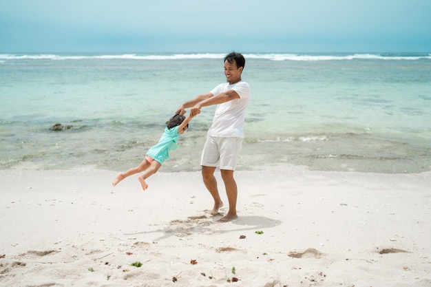 Padre cogidos de la mano de la hija cuando juega swing gira en la playa