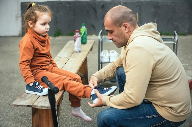 el padre cuida a su pequeña hija, pone sus zapatillas de deporte en un paseo