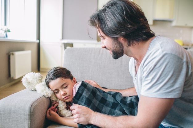 Padre cuidadoso está cubriendo a su hija con una manta