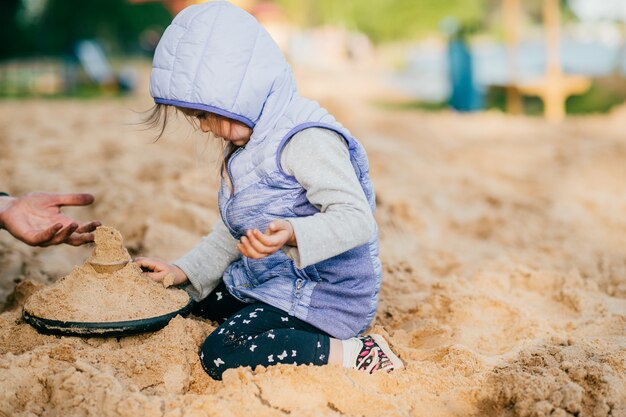 Padre cuidando y jugando con su encantadora hija en la playa en el patio de recreo para niños. Familia de estilo de vida feliz juntos en verano en la naturaleza más allá del mar