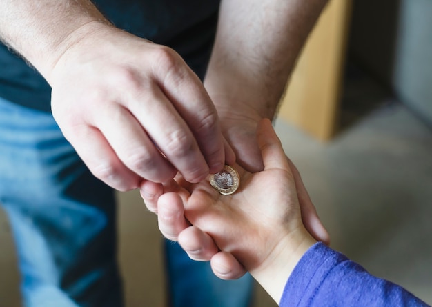 Padre dando una moneda de una libra a su hijo, vista de cultivo de la mano del hombre de los niños poniendo la mano del niño mony coinon. Los padres dan dinero al niño.