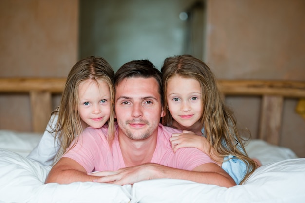 Padre con dos adorables niñas divirtiéndose en la cama sonriendo