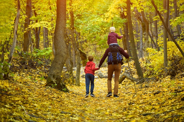 Padre y dos hijos caminando en el bosque de otoño.