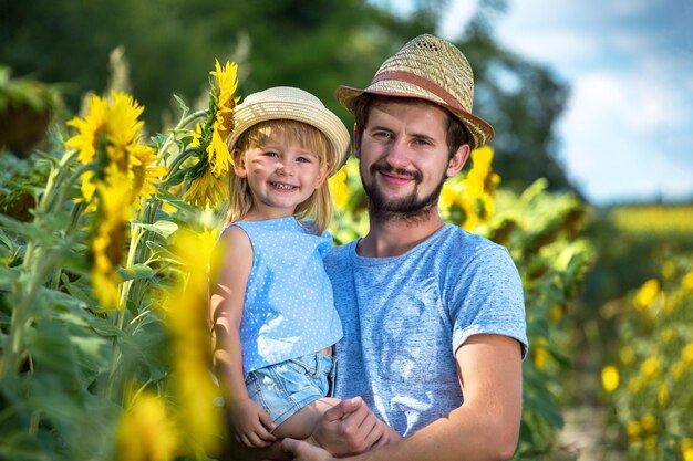 Padre e hija se abrazan en el campo de girasoles mirando a la cámara