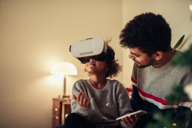 Padre e hija afroamericanos disfrutan usando auriculares de realidad virtual en casa