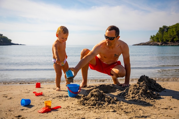 Padre e hija construyendo castillos de arena en la playa en día soleado