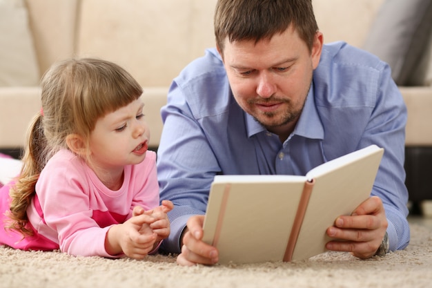 Padre e hija se encuentran en el piso leyendo libros interesantes juntos