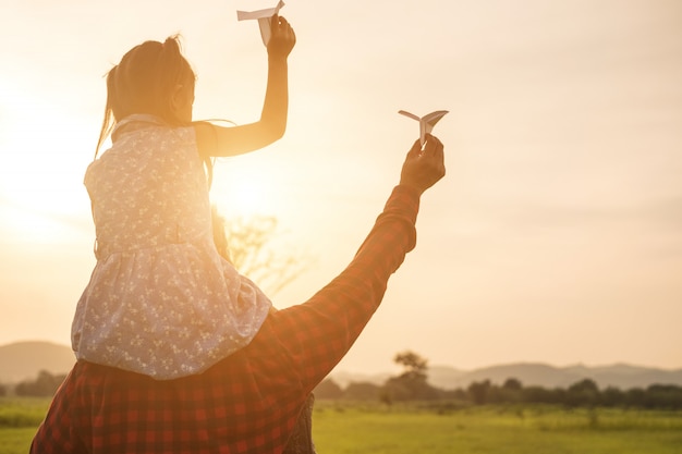 Padre e hija están contentos con el avión de papel en el prado.