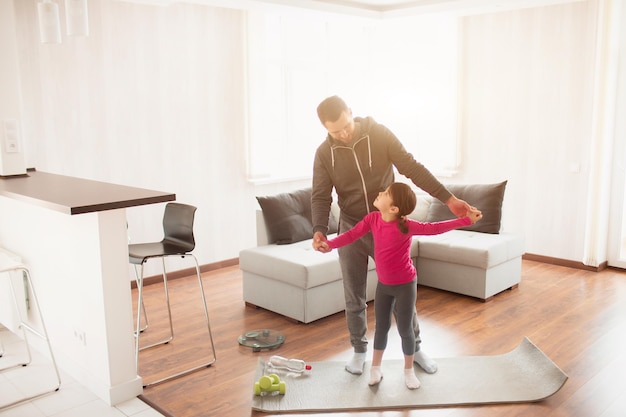 Padre e hija están entrenando en casa. Entrenamiento en el apartamento. Deportes en casa. Están de pie sobre una estera de yoga.