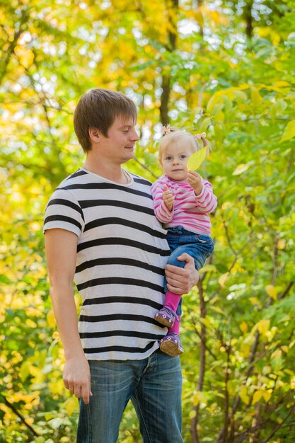 Padre e hija de familia a dar un paseo por el parque en otoño. El niño está en las manos seguras del padre.