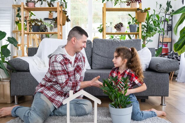 Padre e hija de familia incompleta disfrutan de un nuevo hogar sentados en el sofá Seguro hipotecario y protección comprando y mudándose a su propia casa invernadero con planta en maceta