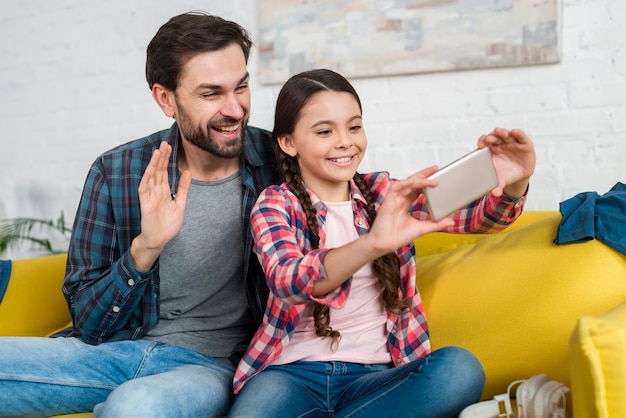 Foto padre e hija hablando con alguien en video llamada