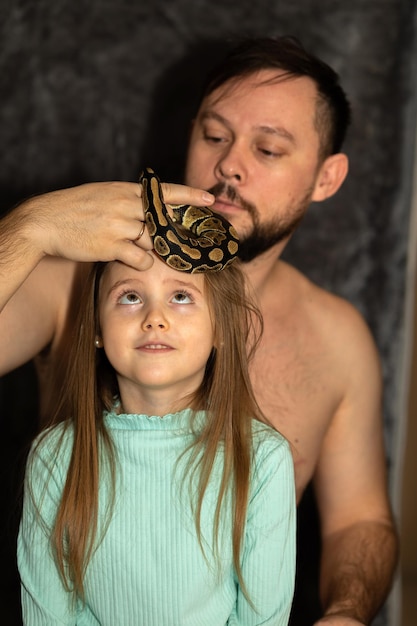 Foto padre e hija jugando con una serpiente retrato de una niña sonriente de verde y un hombre sosteniendo una serpe