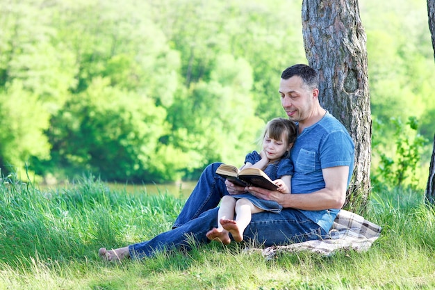 Padre e hija leyendo el libro de la biblia en la naturaleza