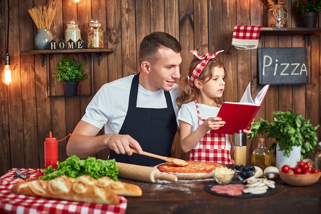 Padre e hija leyendo el libro de recetas mientras cocina pizza