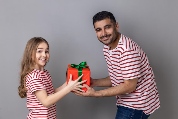 Padre e hija mirando a la cámara con feliz expresión de papá dando un regalo de cumpleaños a un niño