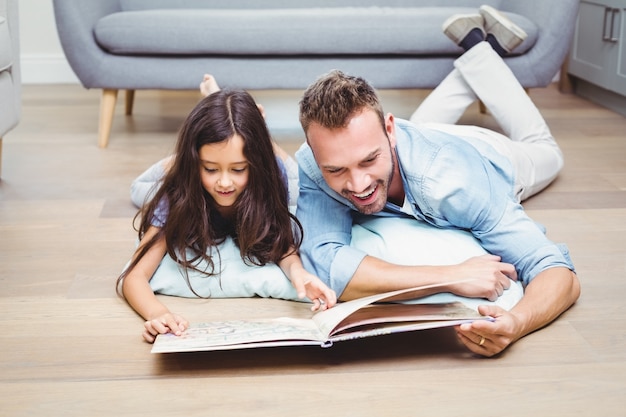 Padre e hija mirando en libro ilustrado en el piso