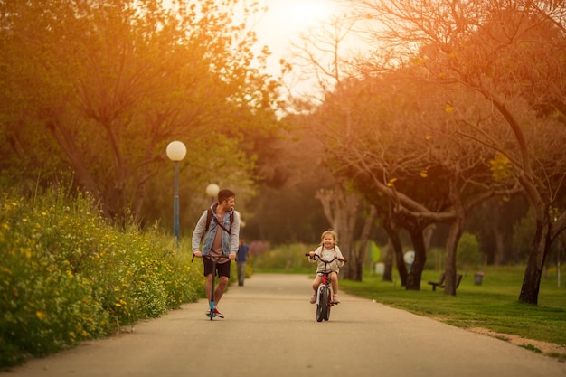 Padre e hija pequeña montando scooter y bicicleta tiempo en familia