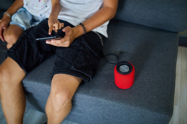 Padre e hija probando hablando altavoz inalámbrico inteligente, controlando dispositivos domésticos con comandos de voz, sentado en el sofá en casa, concepto de hogar inteligente