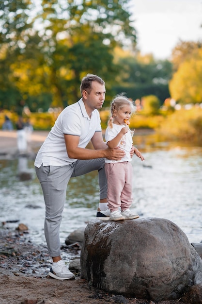 Padre e hija rubia linda juntos en el verano en el parque en la naturaleza niña comiendo piruleta