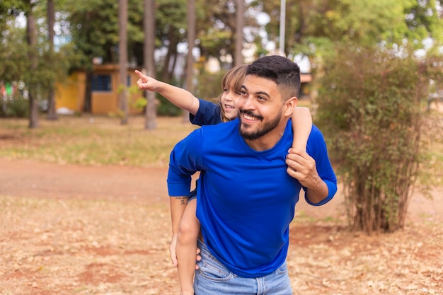 Padre e hija sonriendo a la cámara en el parque Hija sube a la espalda de papá Feliz Día del Padre