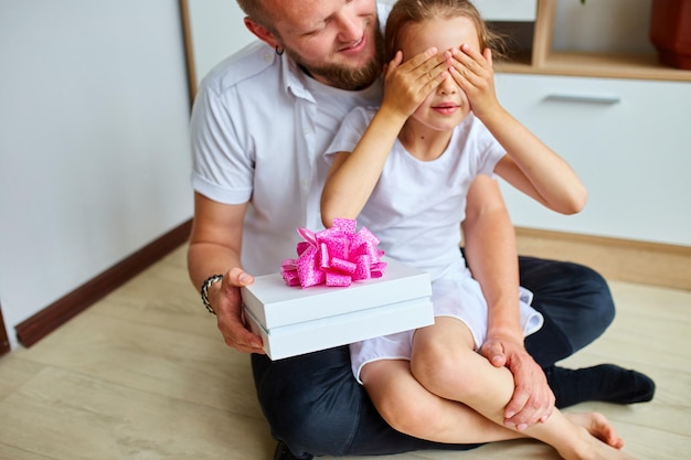 Padre e hija sonrientes compartiendo una caja de regalo con un lazo rosa en el interior