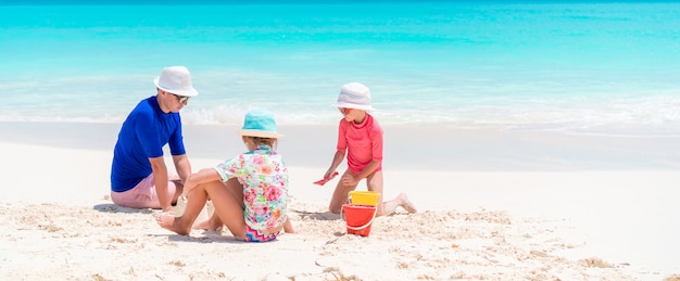 Padre e hijas haciendo castillos de arena en playa tropical