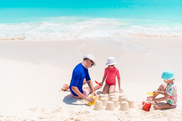 Padre e hijas haciendo castillos de arena en playa tropical