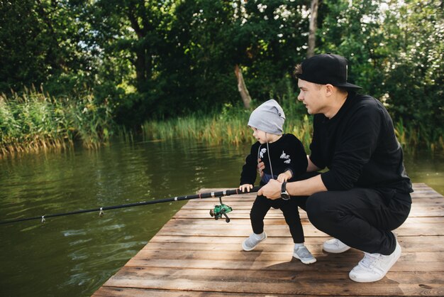 Padre e hijo de un año lindo pesca con una caña de pescar en la naturaleza. El concepto de escapada rural. Artículo sobre el día de pesca.