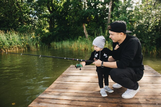 Padre e hijo de un año lindo pesca con una caña de pescar en la naturaleza. El concepto de escapada rural. Artículo sobre el día de pesca.