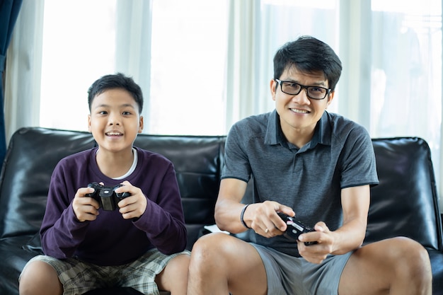 Padre e hijo asiáticos disfrutan jugando videojuegos junto con un joystick de video con emoción y muy divertido en la sala de estar en casa